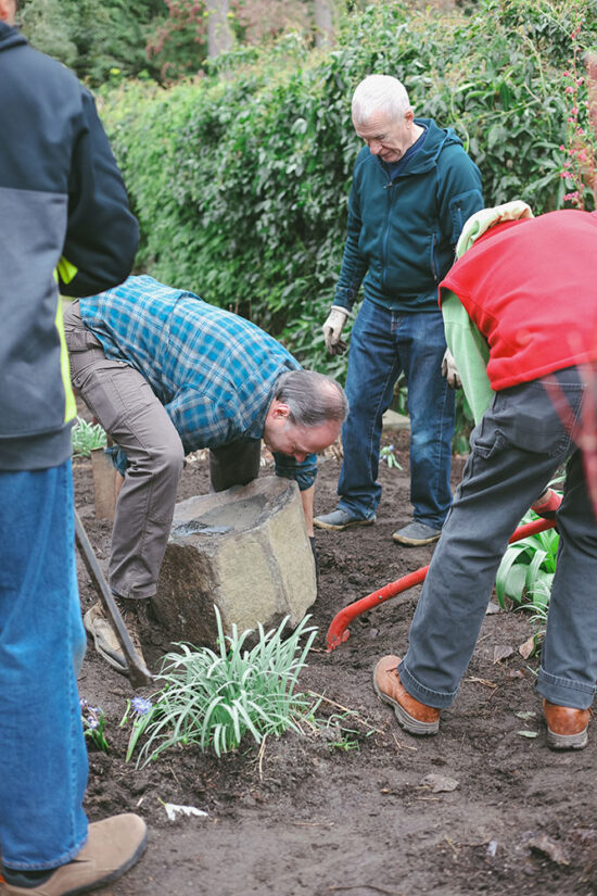 Volunteers installing a shallow stone water basin among newly planted perennials in the Habitats at Home exhibit.